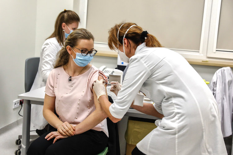 Kobieta w jasnej koszulce jest szczepiona przeciwko COVID-19