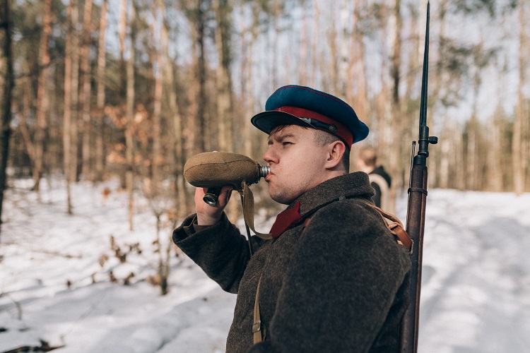 Młody mężczyzna przebrany za żołnierza Armii Czerwonej pije wodę z manierki