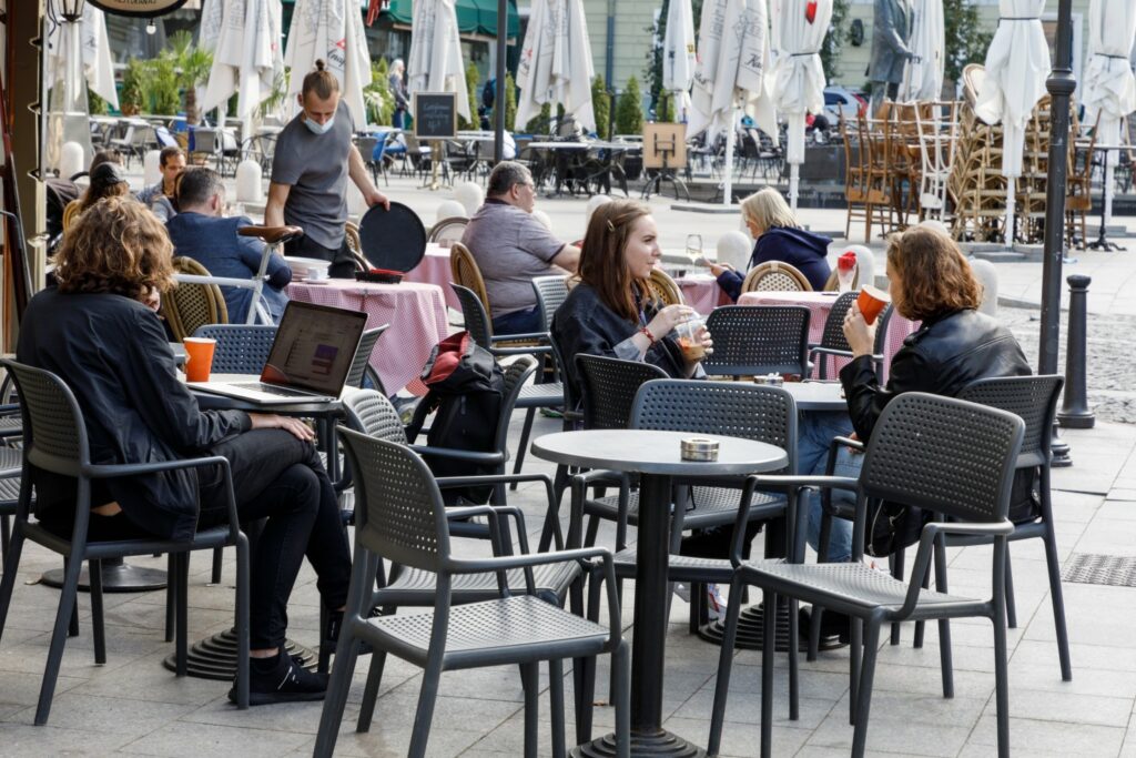 Ludzie siedzą przy stolikach w kawiarni na otwartym powietrzu podczas kwarantanny
