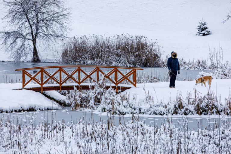 Spacerowicz mija drewniany most nad zaśnieżonym jeziorem