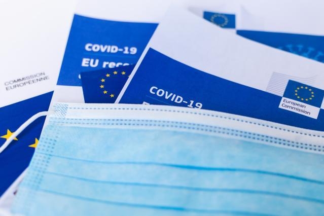 Jednorazowe maski ochronne leżą na unijnych broszurach dotyczących zwalczania COVID-19