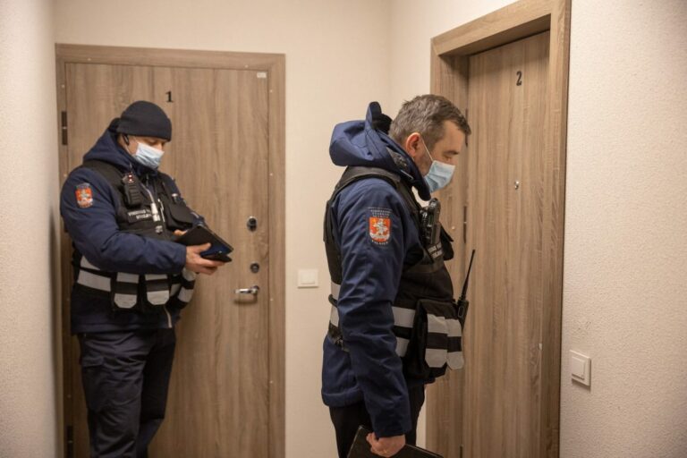 Dwóch policjantów w mundurach i maskach puka do drzwi mieszkania