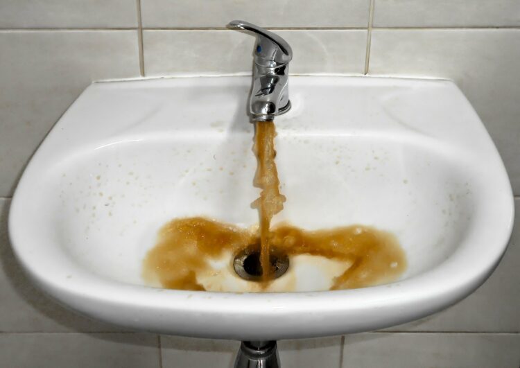 Umywalka, do której leje się zanieczyszczona woda o brunatnym kolorze