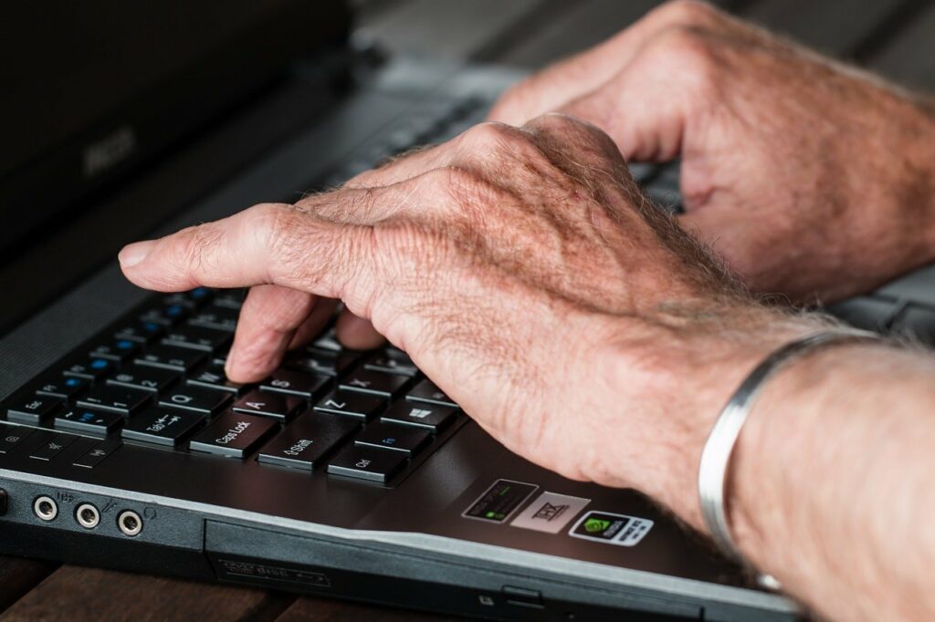 Dłonie starszej osoby piszące na komputerze