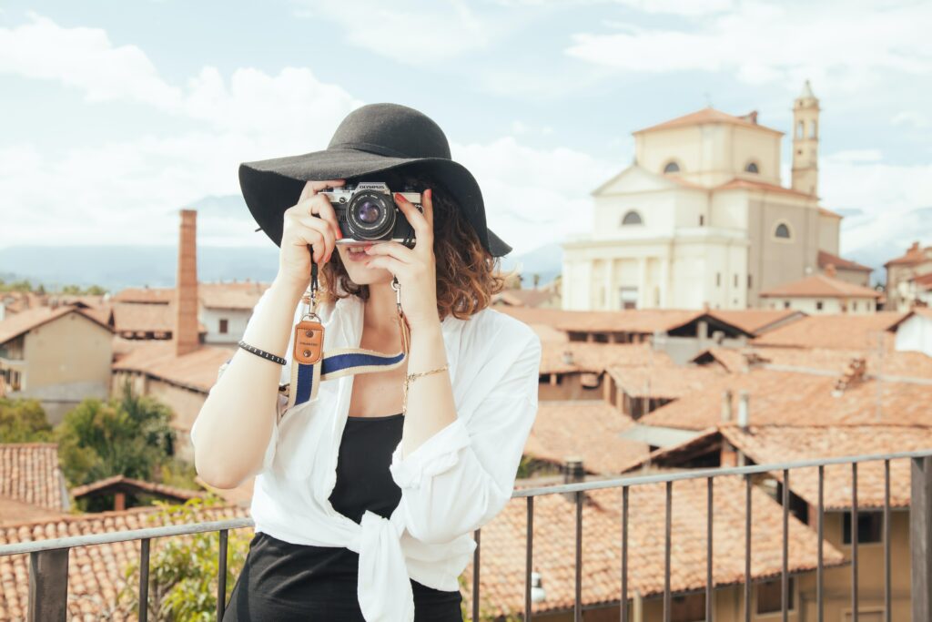 Młoda kobieta w białej koszuli i czarnym kapeluszu robi zdjęcia aparatem fotograficznym