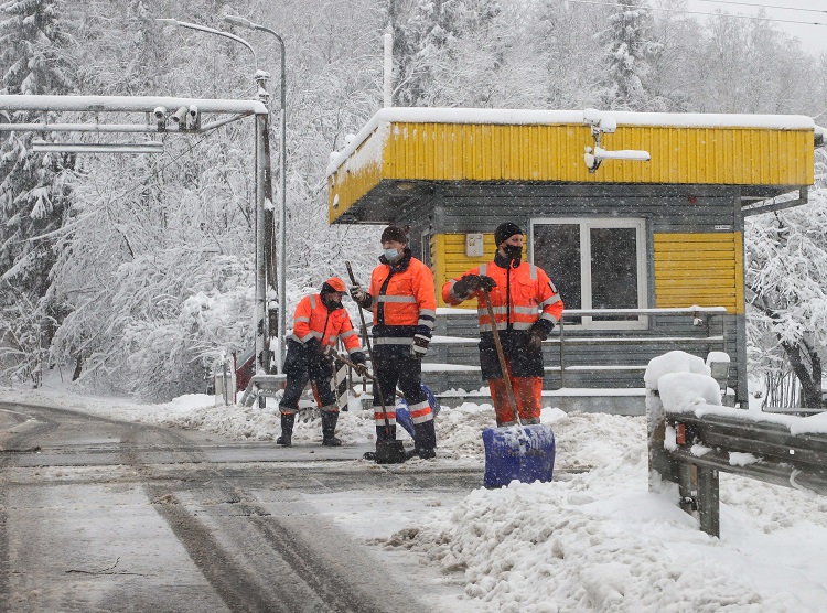 Trzech mężczyzn w oblaskowych pomarańczowych kombinezonach usuwa śnieg z jezdni