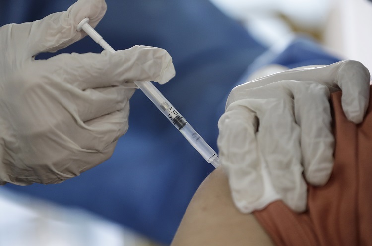 Osoba w białych rękawiczkach ochronnych szczepi pacjenta przeciwko koronawirusowi