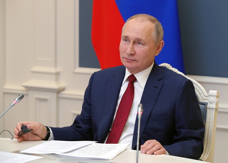 Prezydent Rosji, Władimir Putin, siedzi przy biurku i patrzy w dal z pobłażliwym uśmiechem