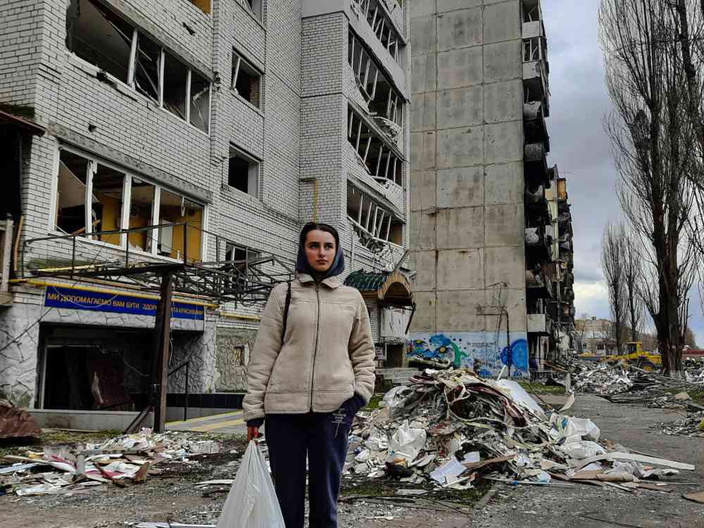 Kobieta stoi na tle zbombardowanej Borodzianki