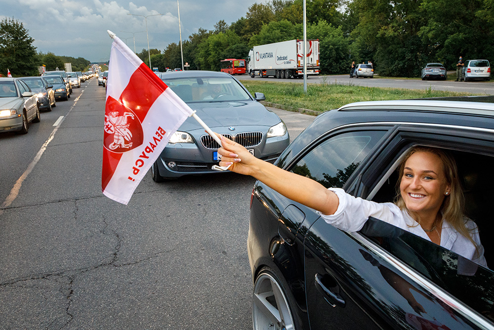 Kobieta jadąca samochodem z chorągiewką Białorusi.