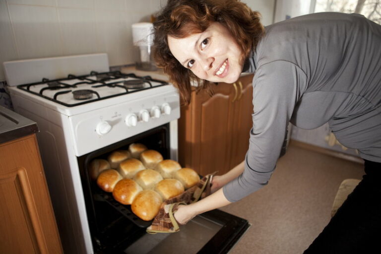 Kobieta piecze bułeczki w piekarniku.