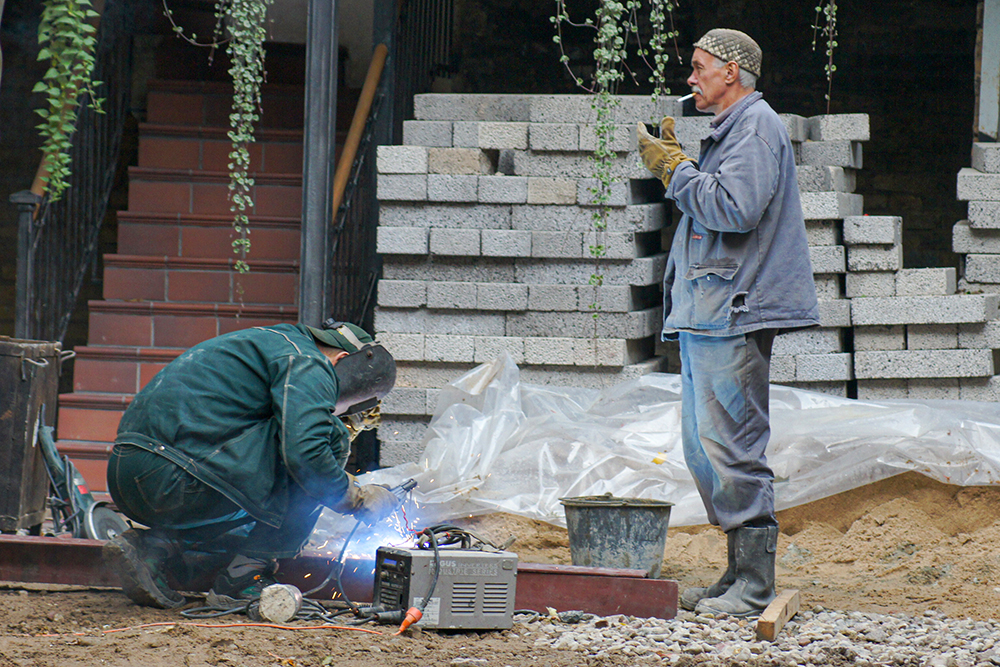 Spawacz i robotnik palący papierosa na budowie.