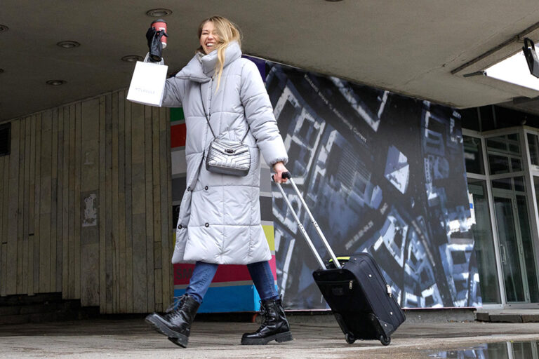 Uśmiechająca się kobieta obładowana walizką.