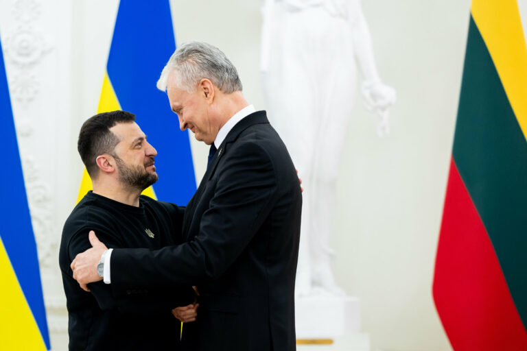 Zełenski ściska się z prezydentem Litwy Gitanasem Nausėdą, uśmiechają się do siebie, w tle widać flagę Litwy i Ukrainy