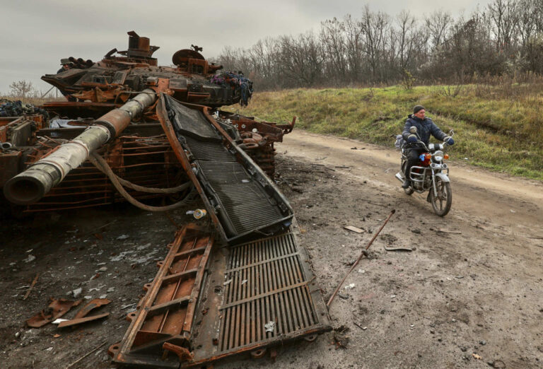 Rozbity czołg i jadący na motocyklu mężczyzna.