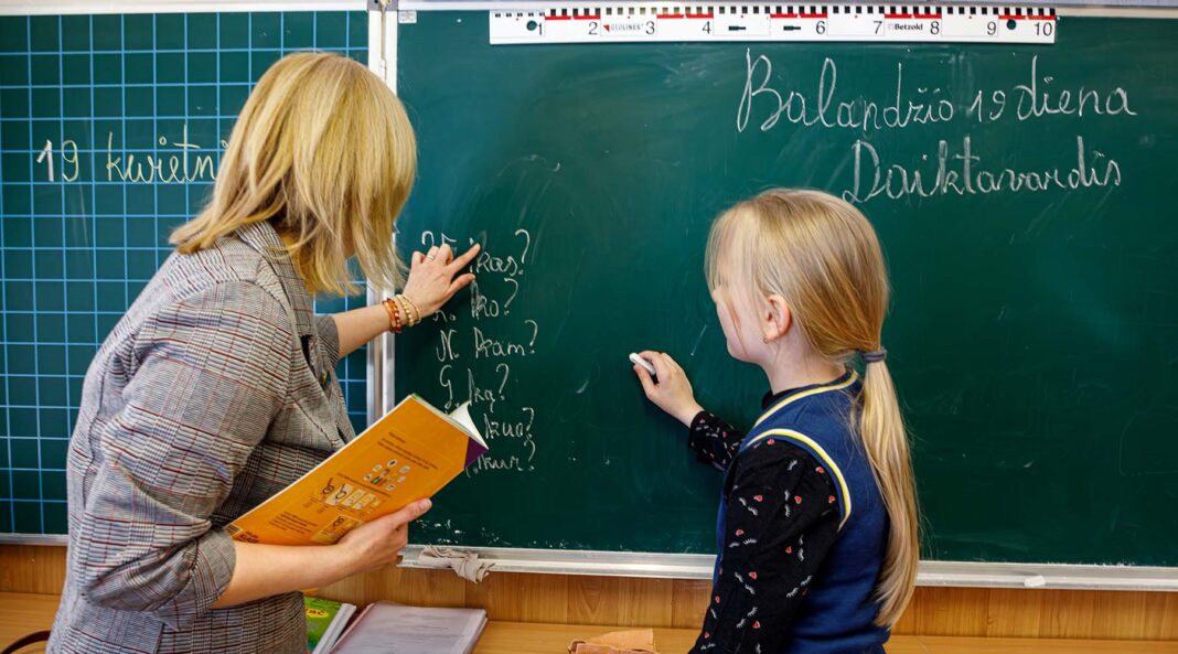 Dziewczynka przy tablicy wraz z nauczycielką na lekcji litewskiego.
