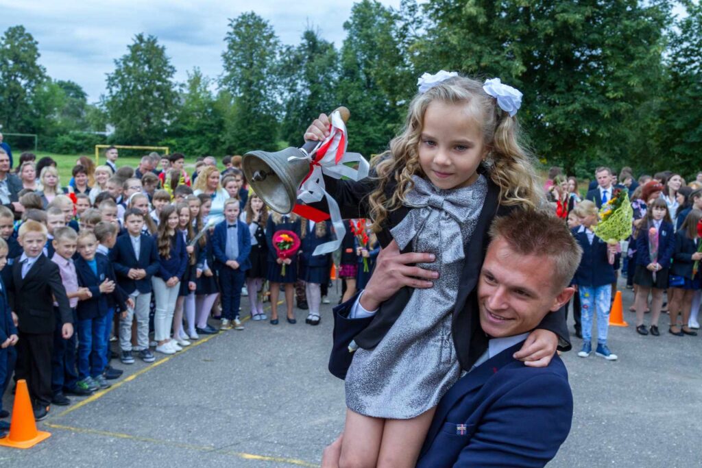 Starszoklasista na ramieniu niesie dziewczynkę z dzwonkiem.