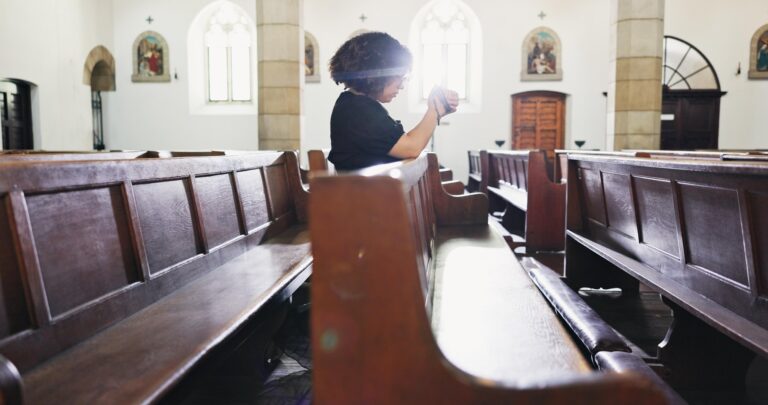 Kobieta odmawia różaniec w kościele.