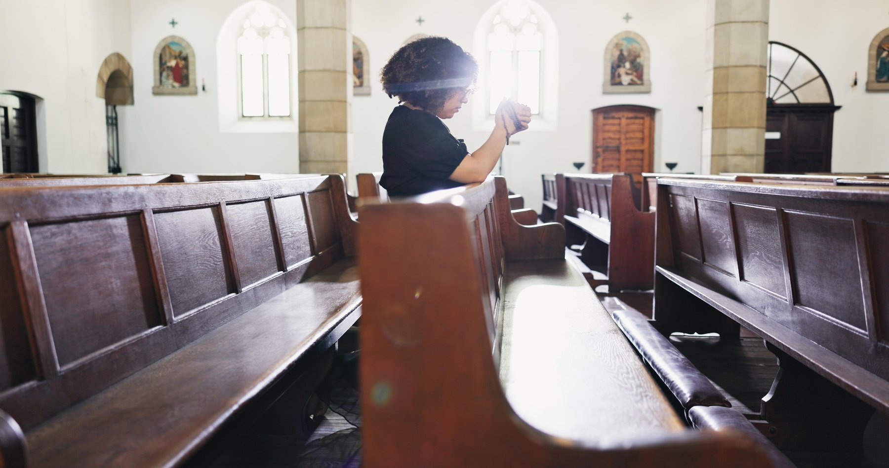 Kobieta odmawia różaniec w kościele.