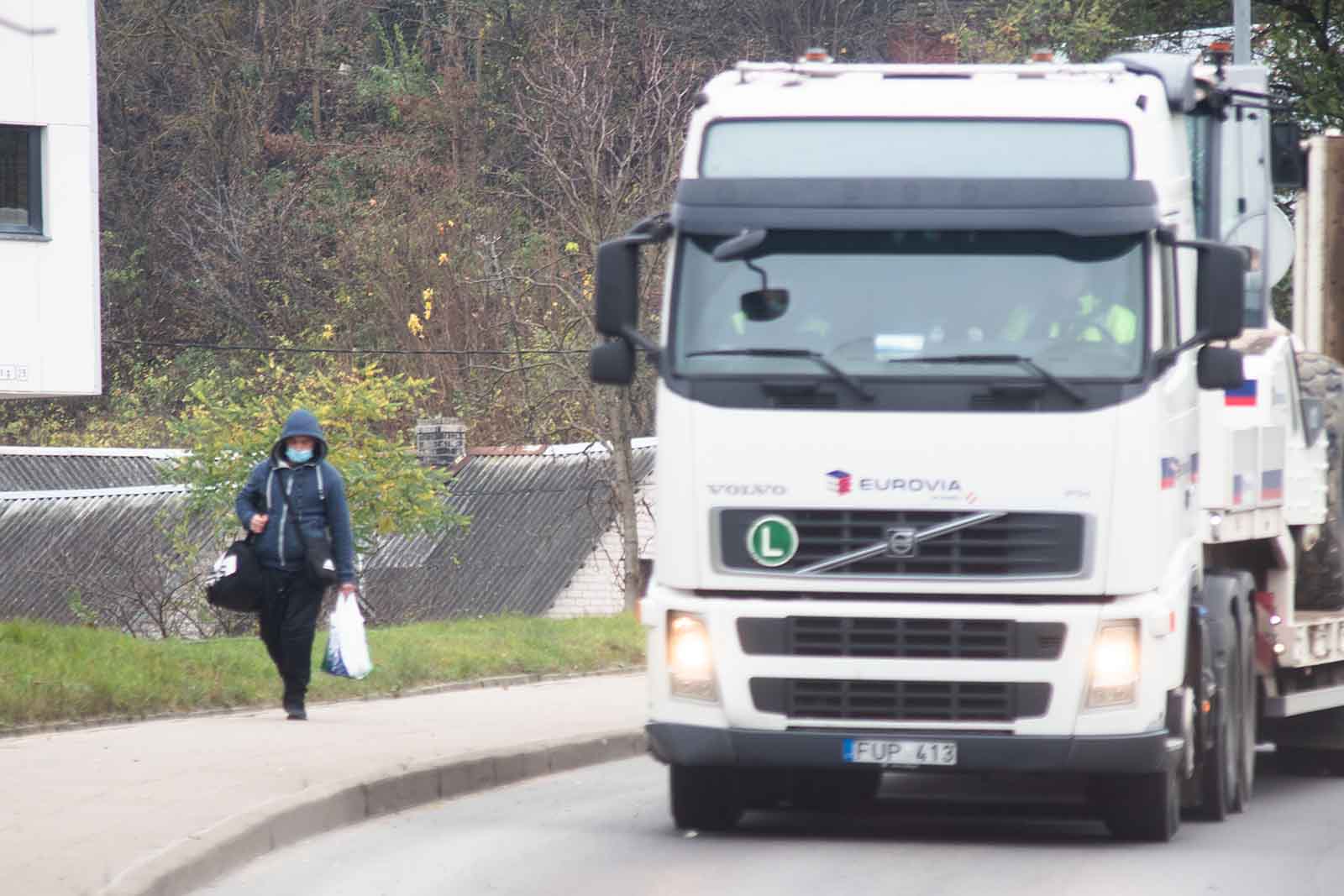 Ciężarówka na drodze, obok idąca kobieta na chodniku.