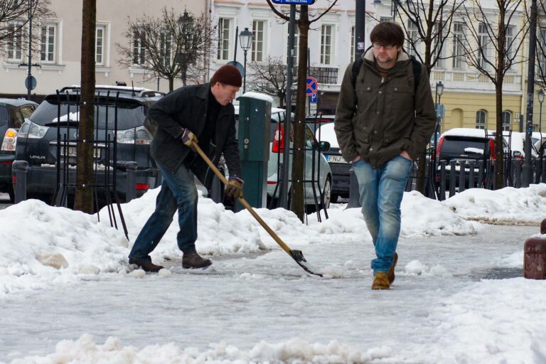 Dozorca szczyści śnieg na chodniku.
