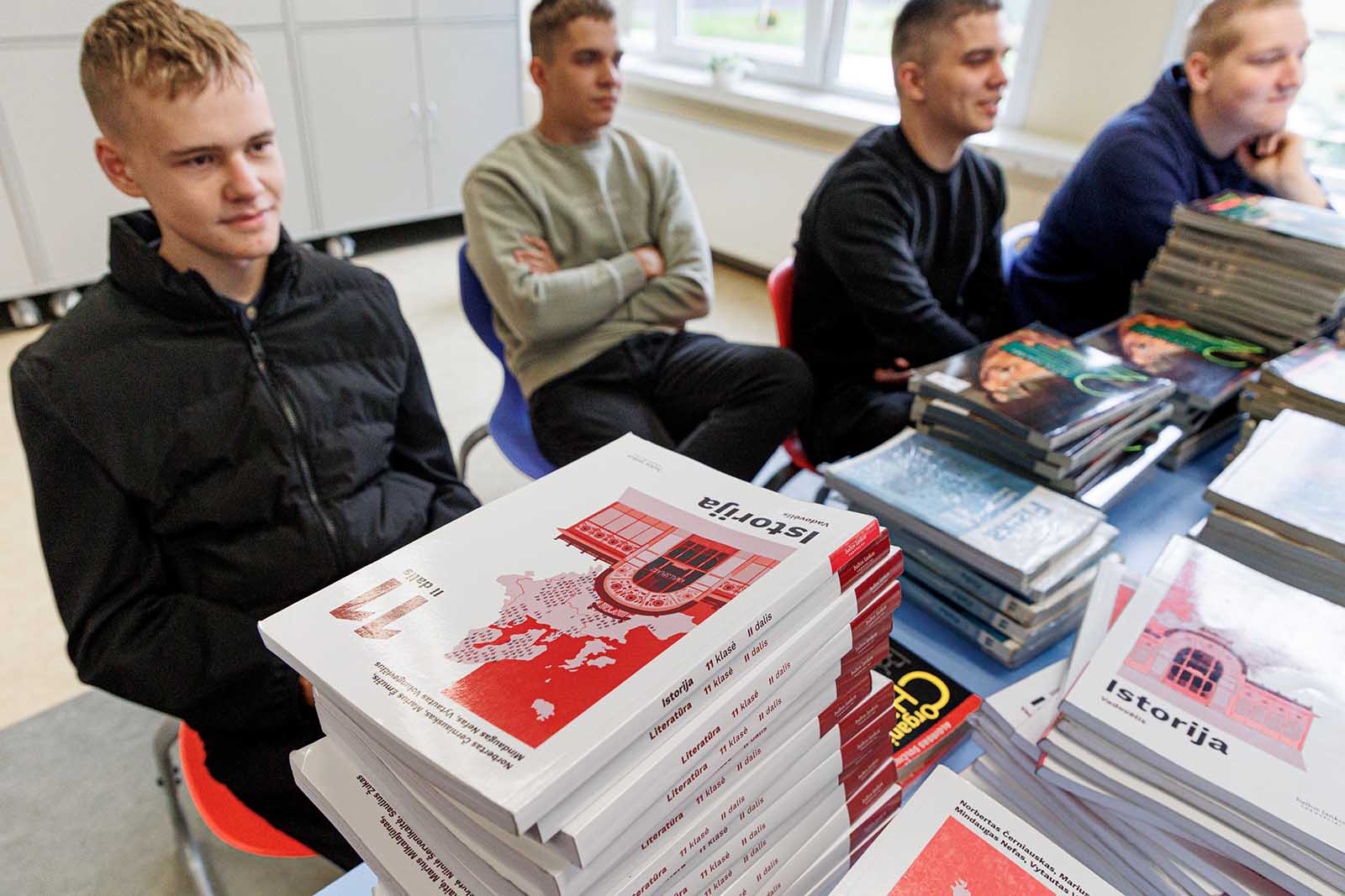 Uczniowie za ławkami obładowanym podręcznikami.