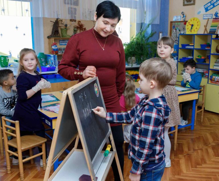 Chłopczyk pisze na tablicy, obok nauczycielka.